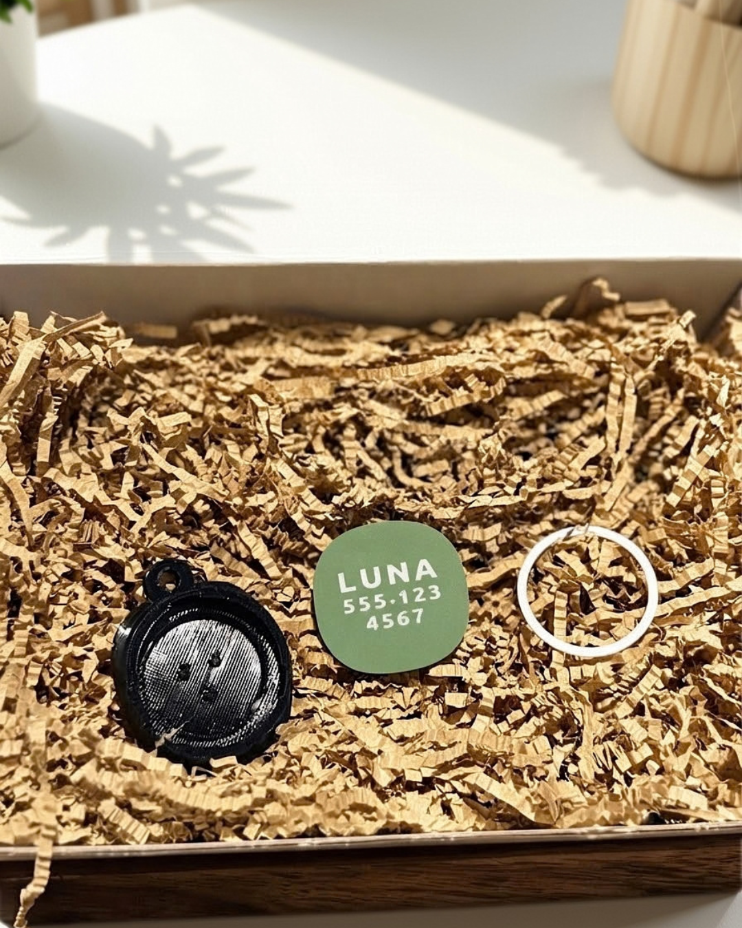 Black TPU AirTag holder base with olive green name plate and split ring, shown separately